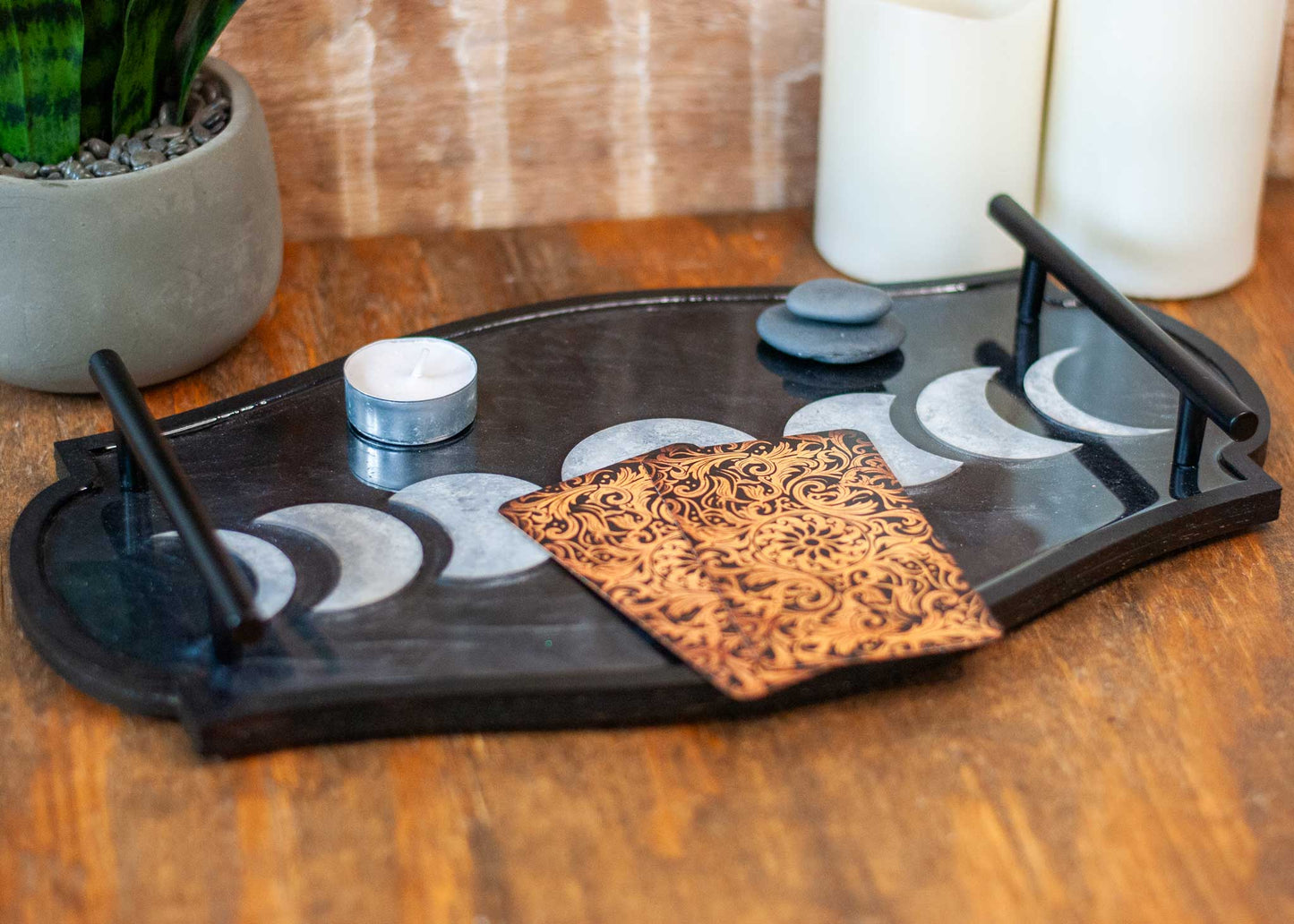 Decorative shimmery black wooden and resin tray with moon phases on a wooden surface with decorate items on top