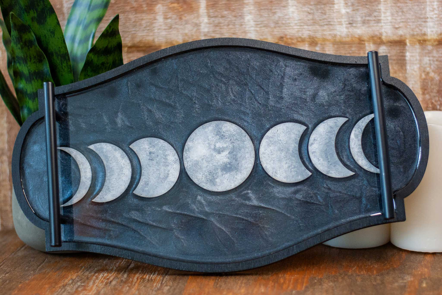 Decorative black and shimmery resin tray with moon phases on a wooden surface