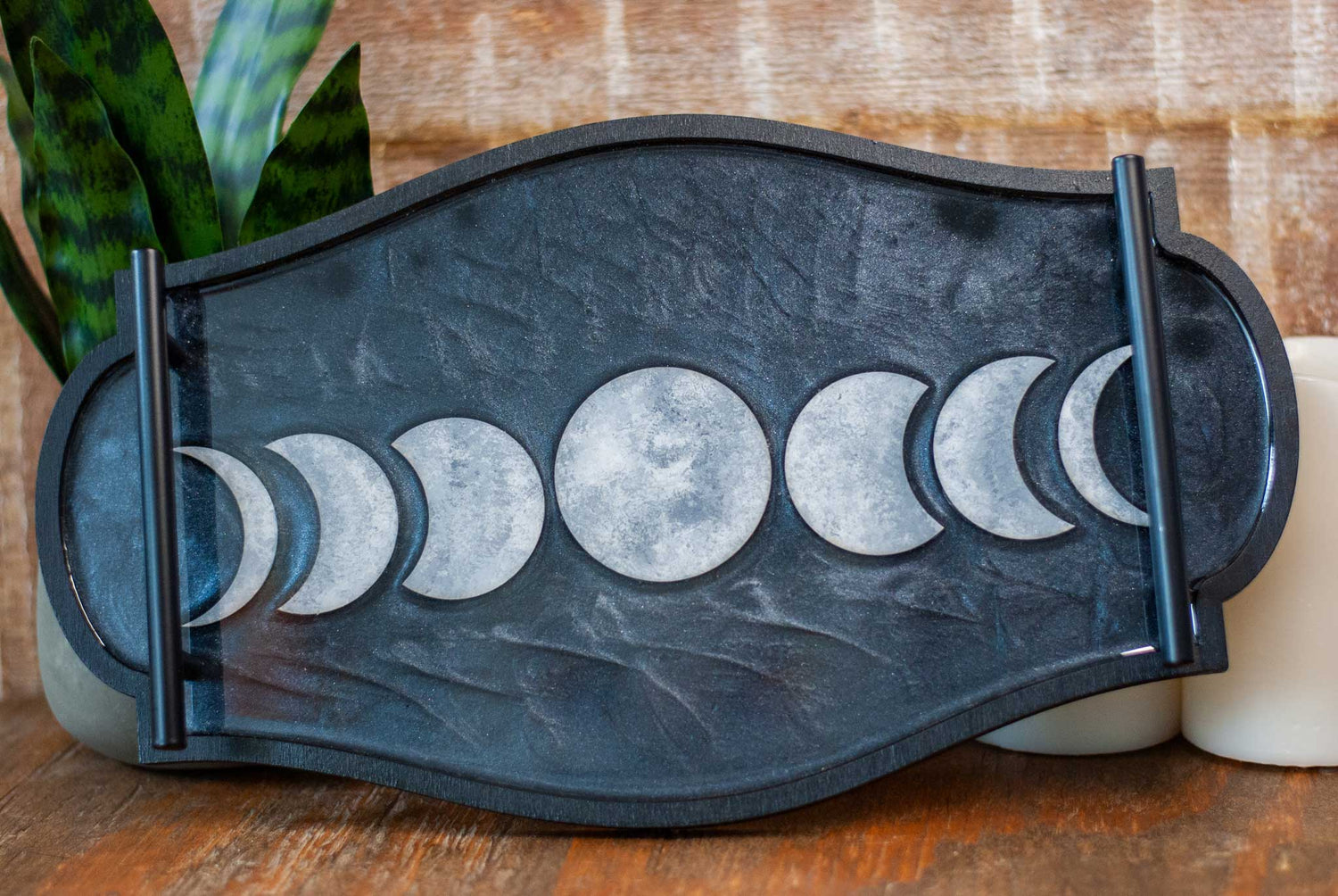Decorative black and shimmery resin tray with moon phases on a wooden surface
