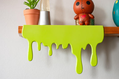 Front view of a green Slime Drip Shelf decor sitting on a wooden floating shelf, 90s Nostalgic shelf sitter, displaying Spooky Season vibes, Halloween Accessories for Bookshelf, Display Shelf, or Mantel, Goosebumps inspired decor