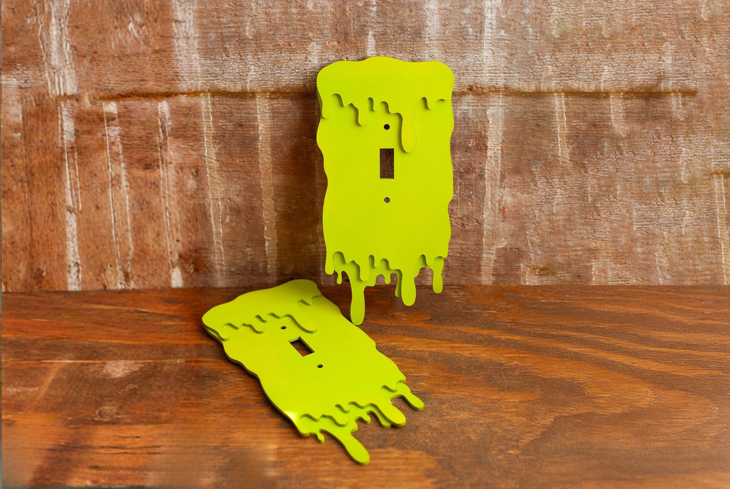 Two green slime drip light switch plate covers on a wooden wall.