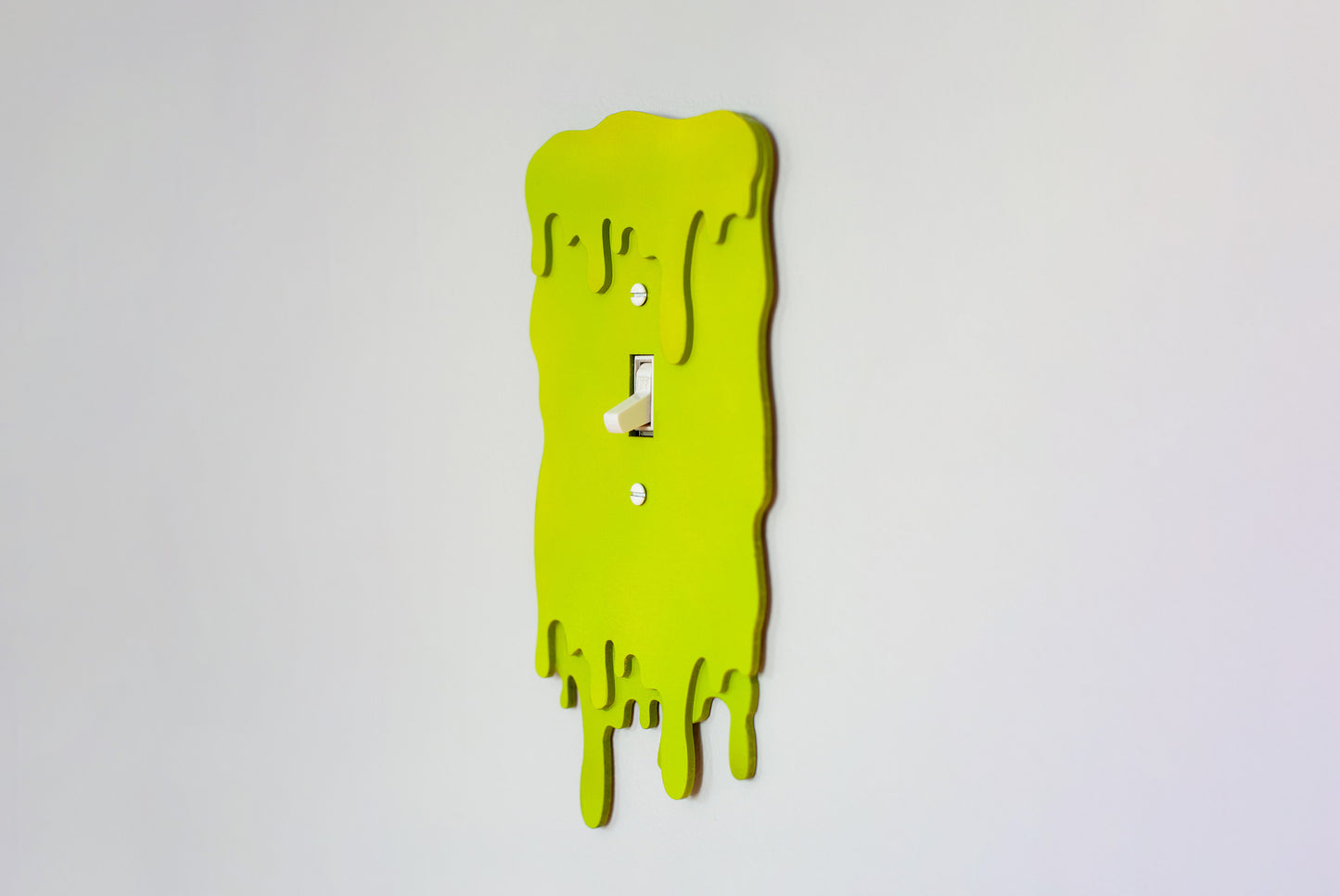 Side view of a green slime drip light switch cover plate on a white wall background