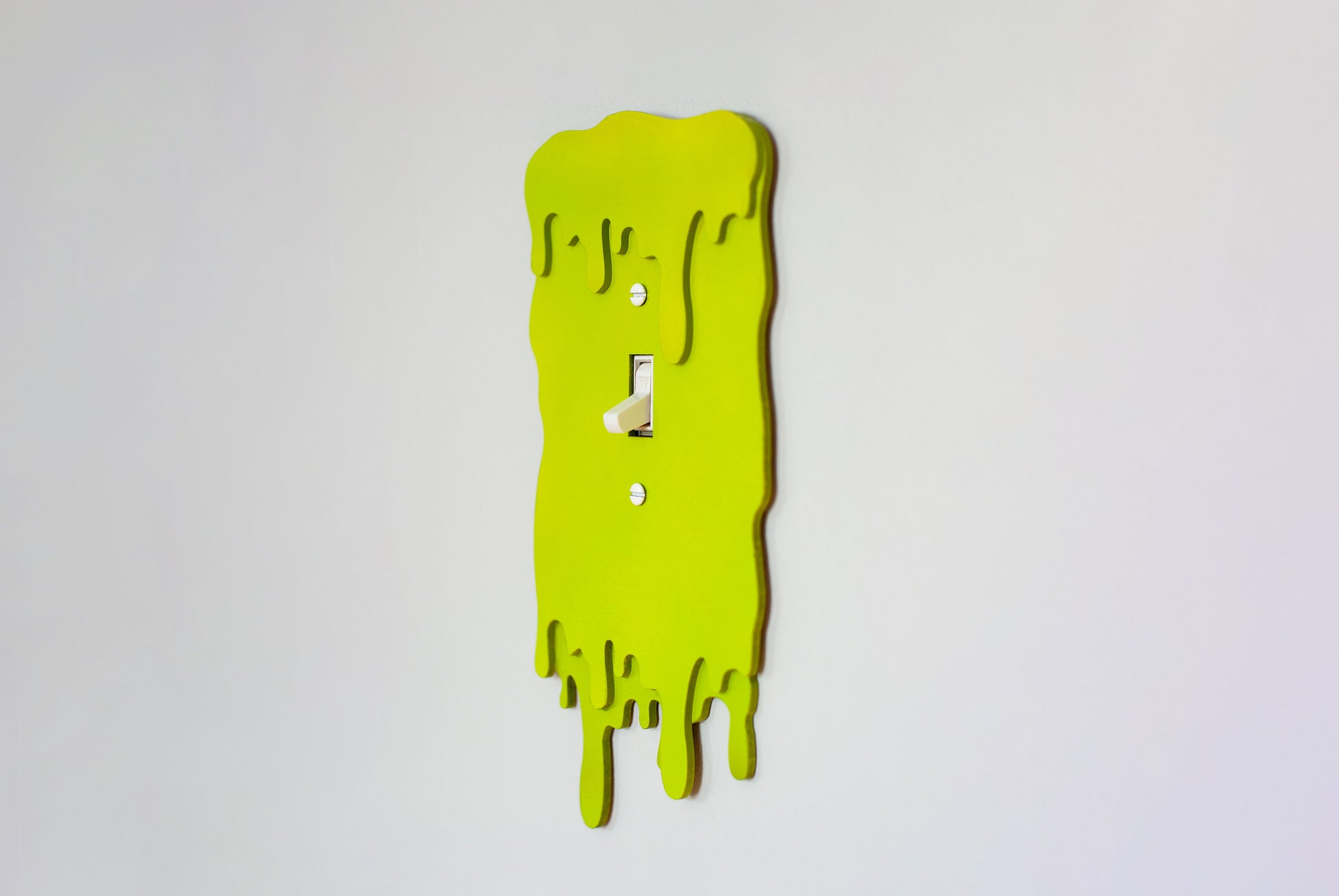 Side view of a green slime drip light switch cover plate on a white wall background