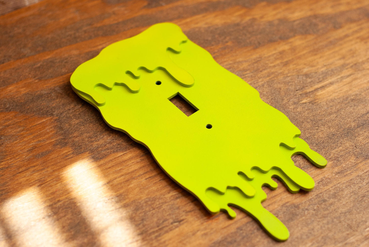Green slime drip light switch plate cover on a wooden table