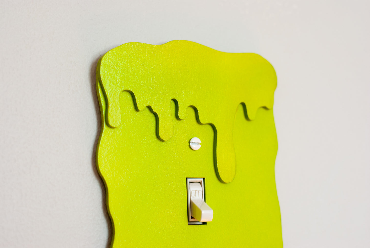 Close up of a green slime drip light switch cover with a unique design on a white background