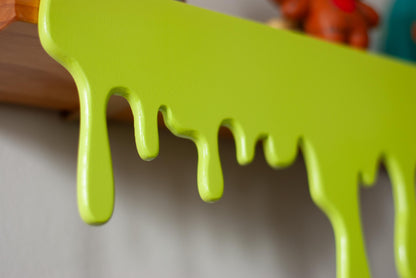 close up view of a green Slime Drip Shelf decor sitting on a wooden floating shelf, 90s Nostalgic shelf sitter, displaying Spooky Season vibes, an Accessory for Bookshelf, Display Shelf, or Mantel, Goosebumps inspired decor