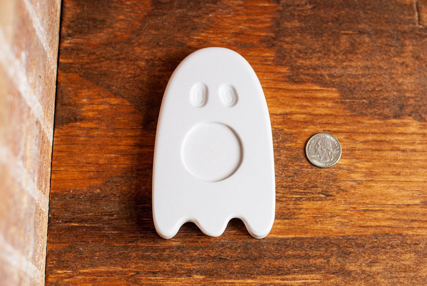 White ghost-shaped tea light holder on a wooden surface with a coin for scale