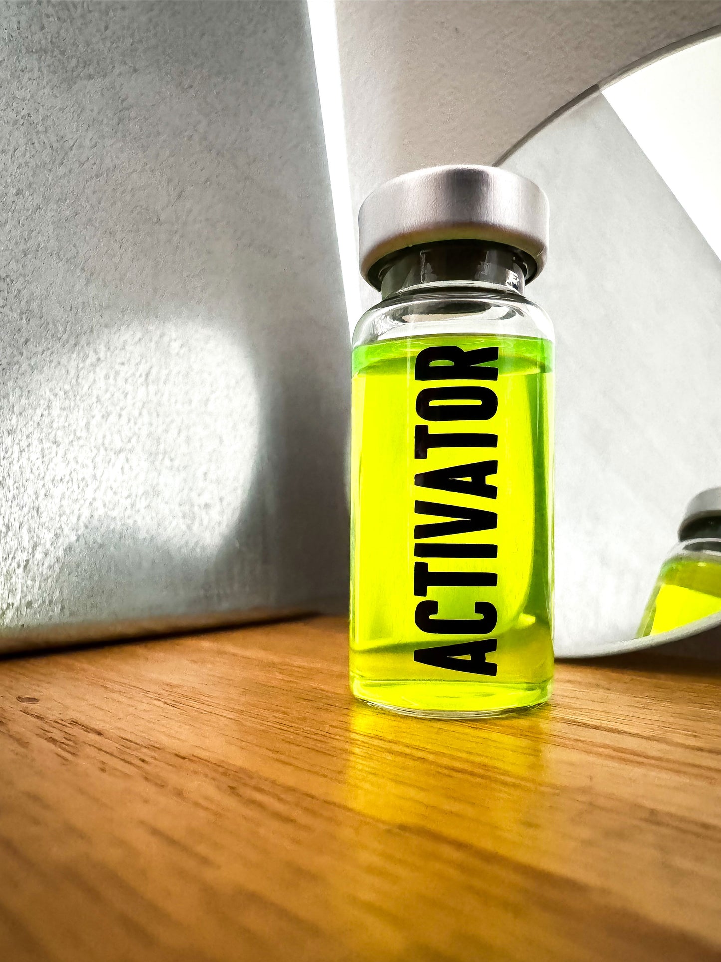 The Substance glass vial movie prop labeled 'ACTIVATOR' with a green liquid  in front of a mirror.