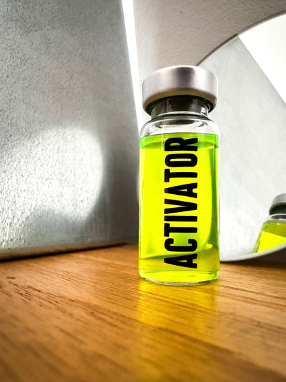 The Substance glass vial movie prop labeled 'ACTIVATOR' with a green liquid  in front of a mirror.