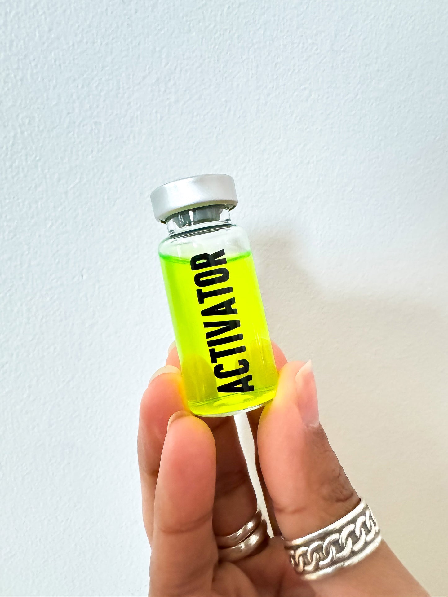 Hand holding a small bottle of The Substance Activator movie prop with 'Activator' label against a light background