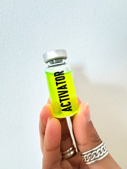 Hand holding a small bottle of The Substance Activator movie prop with 'Activator' label against a light background