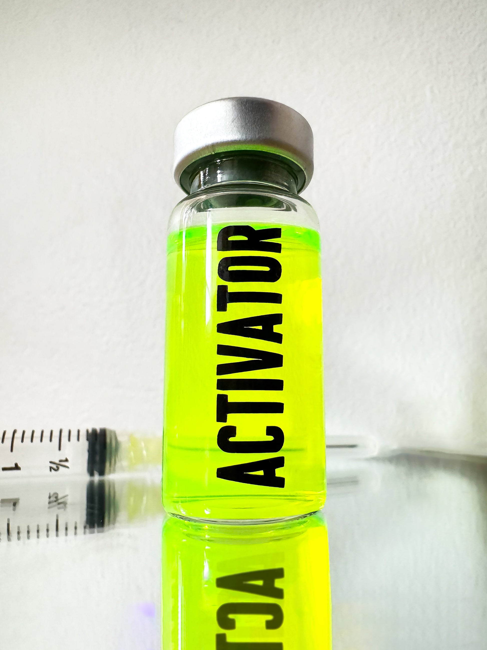 The Substance glass vial movie props labeled 'ACTIVATOR' with a green liquid and syringe on a reflective surface.