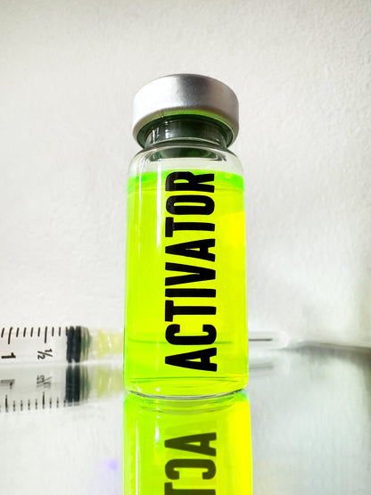 The Substance glass vial movie props labeled 'ACTIVATOR' with a green liquid and syringe on a reflective surface.