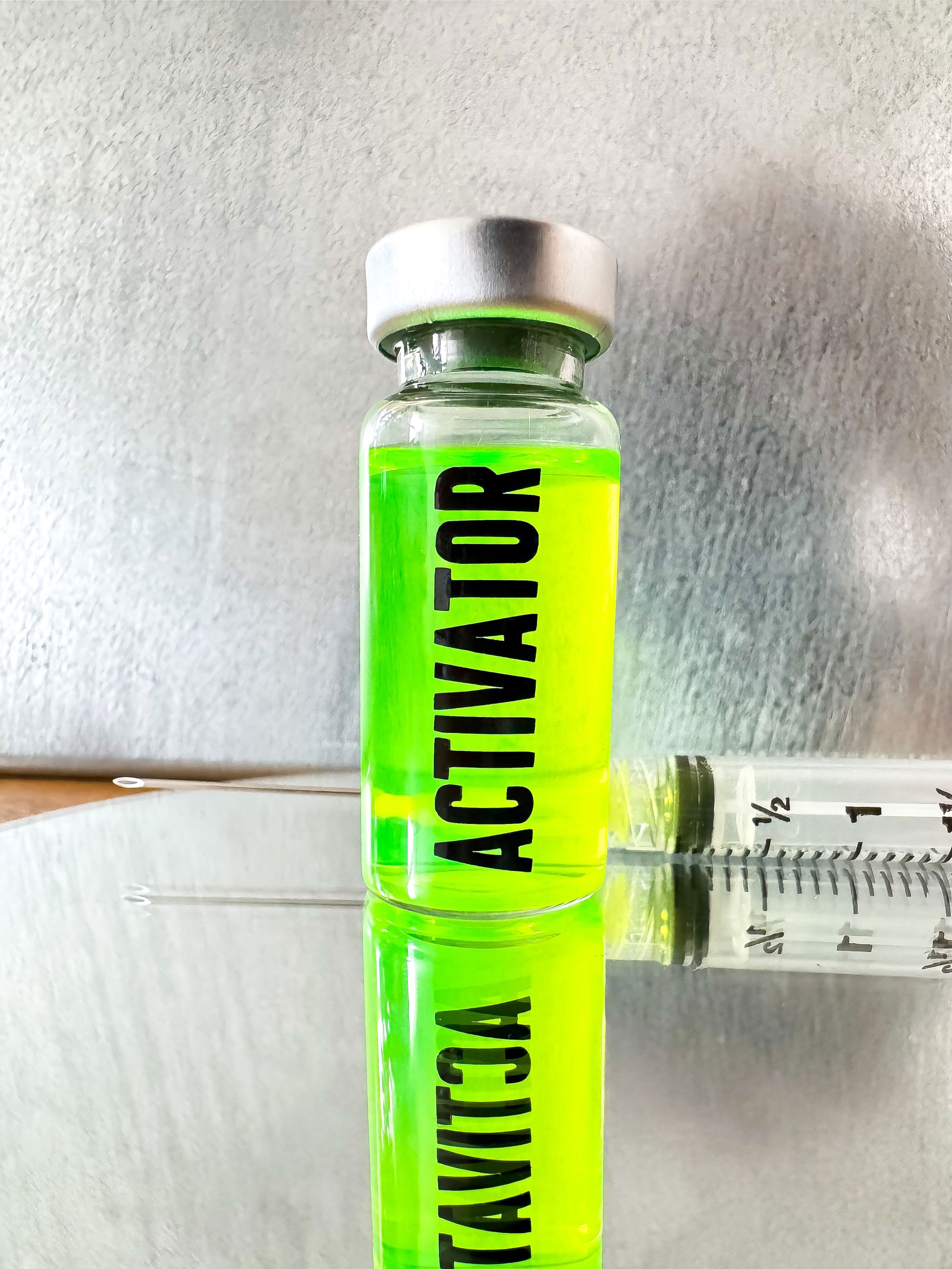 The Substance glass vial movie prop labeled 'ACTIVATOR' with a green liquid and syringe on a metallic surface.