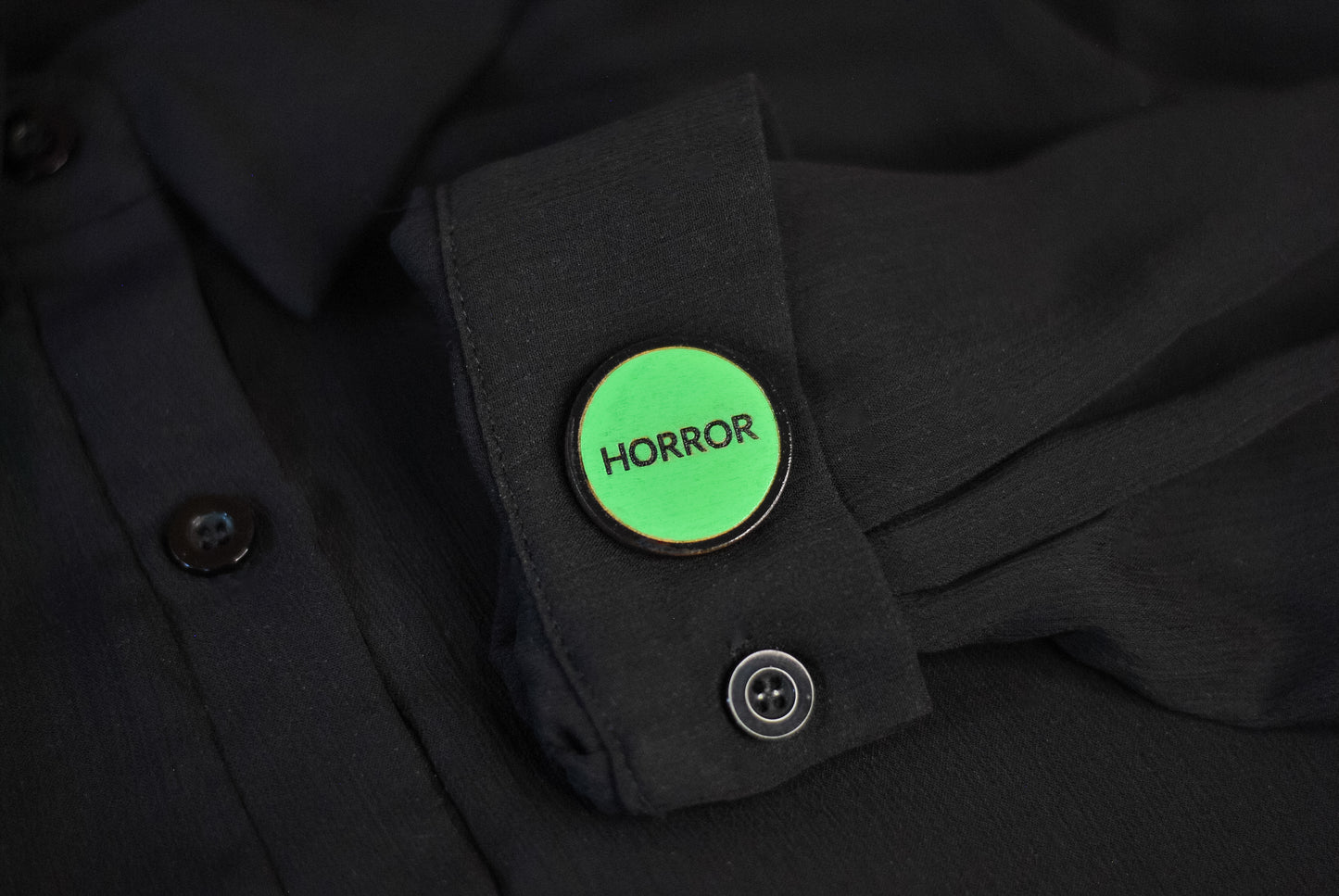 Green retro vhs label horror pinback style button that reads 'Horror' on a black shirt