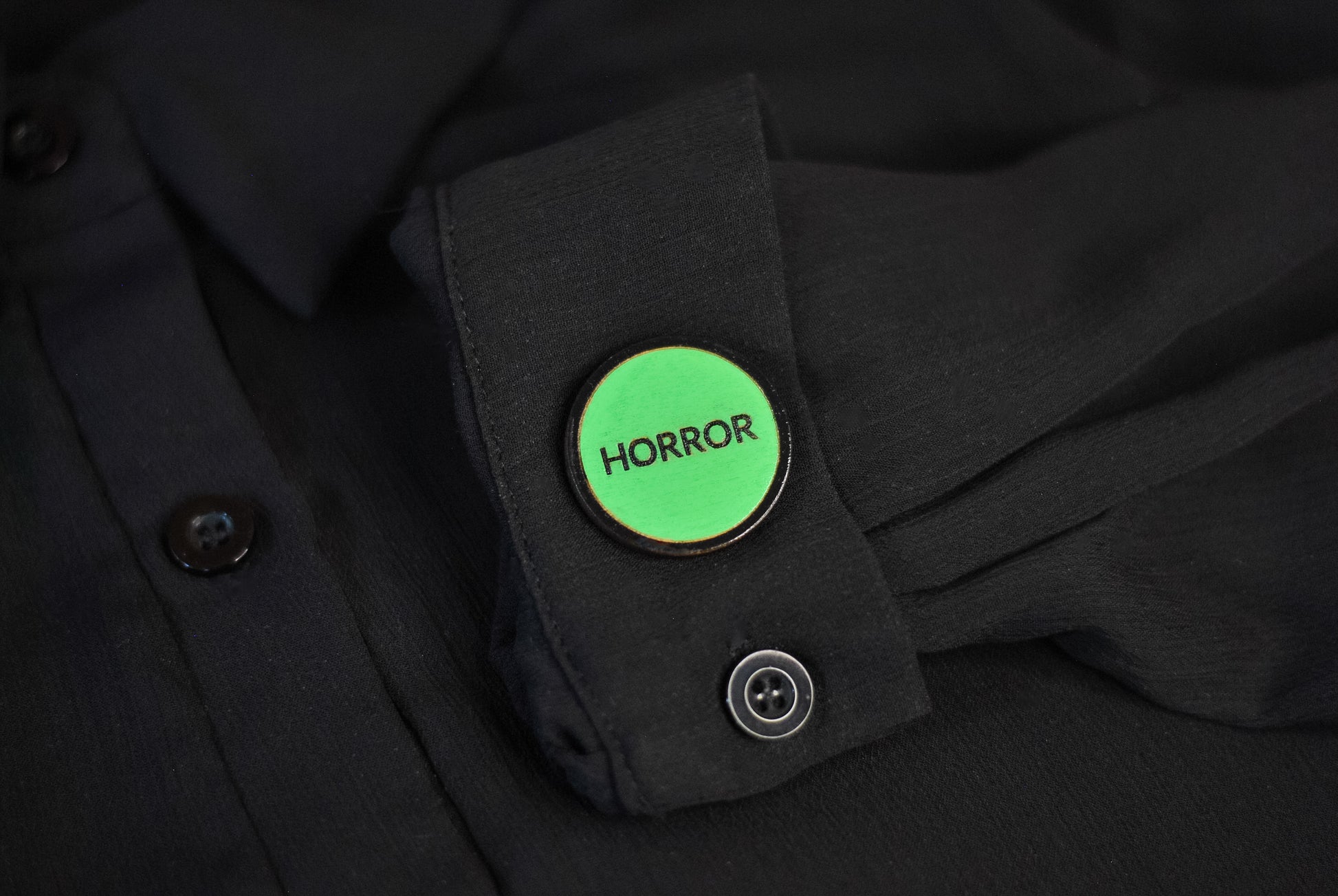 Green retro vhs label horror pinback style button that reads 'Horror' on a black shirt