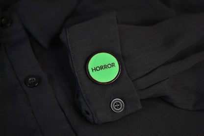 Green retro vhs label horror pinback style button that reads 'Horror' on a black shirt