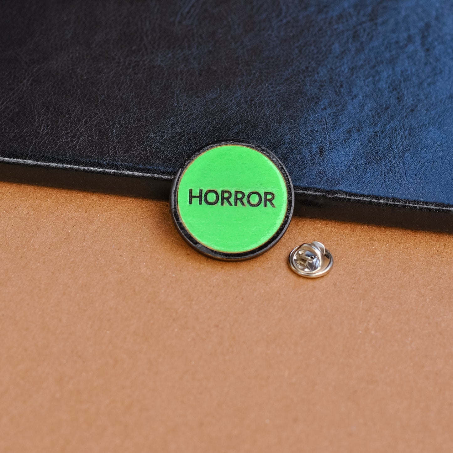 Green retro vhs label horror pinback style button that reads 'Horror' on a leather surface