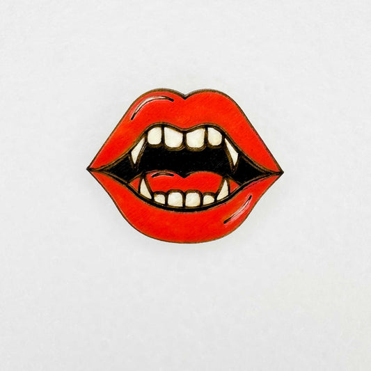 Lip-shaped lapel pin accessory with vampire teeth design on a white background 